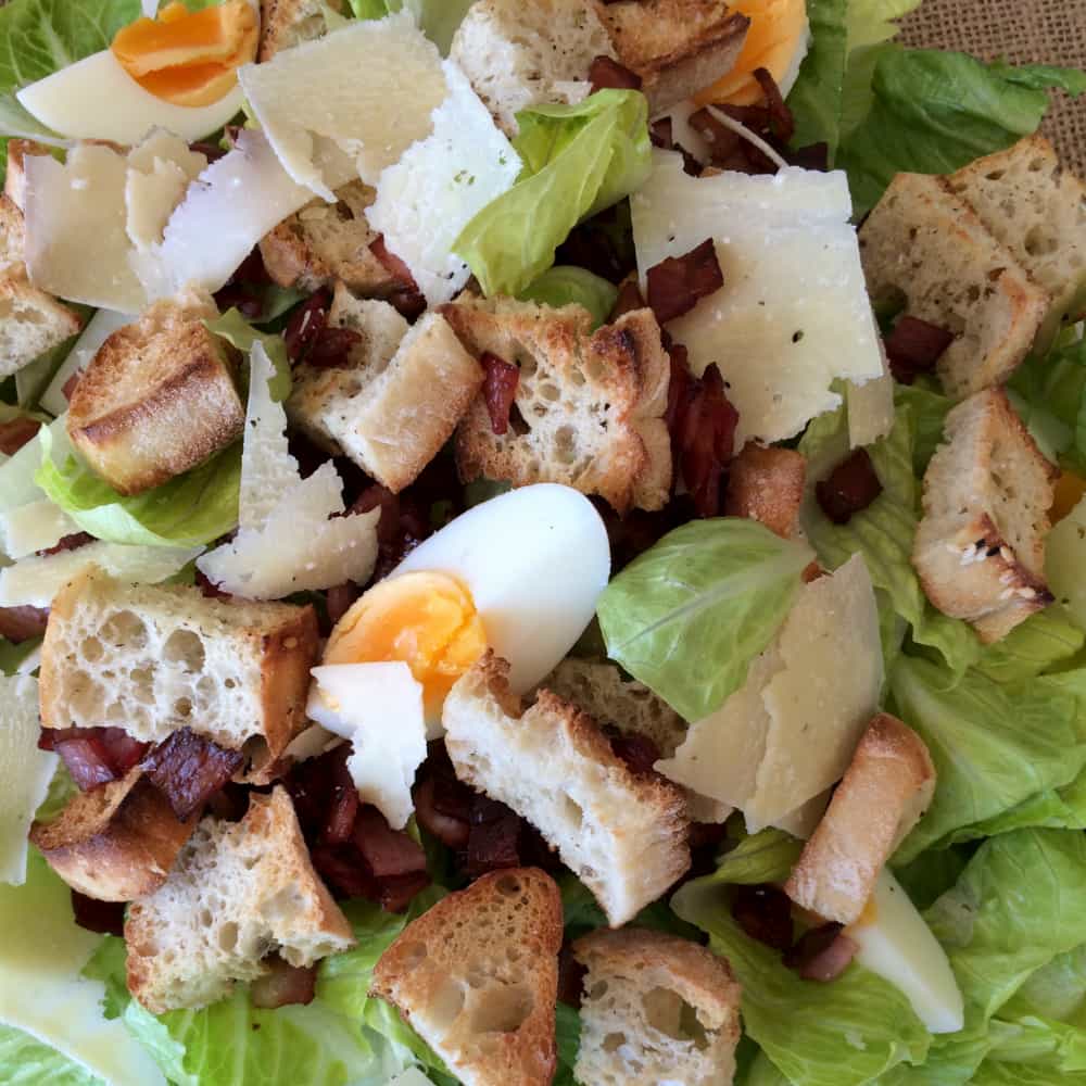 A bowl of lettuce, solf boiled eggs, bacon bits and croutons.