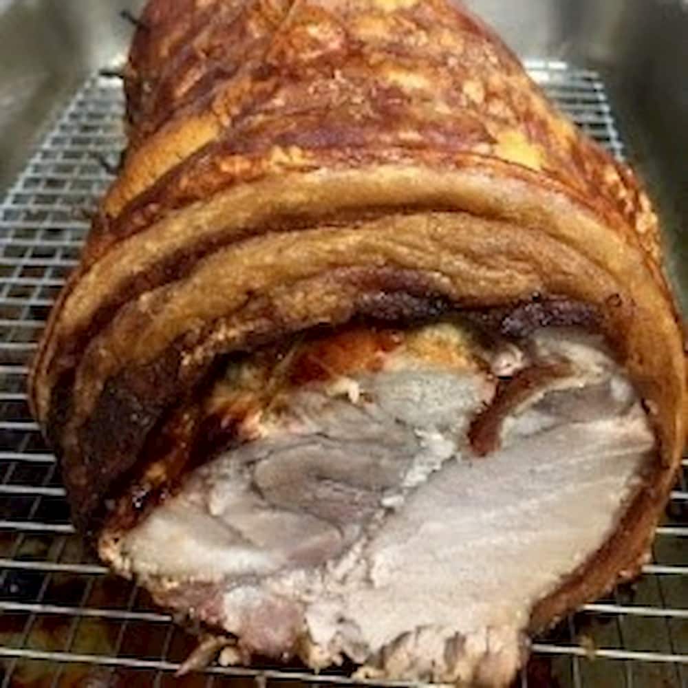 A rolled roast pork with crackling on a wire rack.