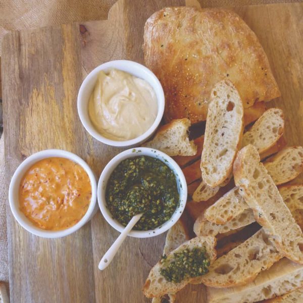 A wooden platter with sliced Turkish bread and three dips.
